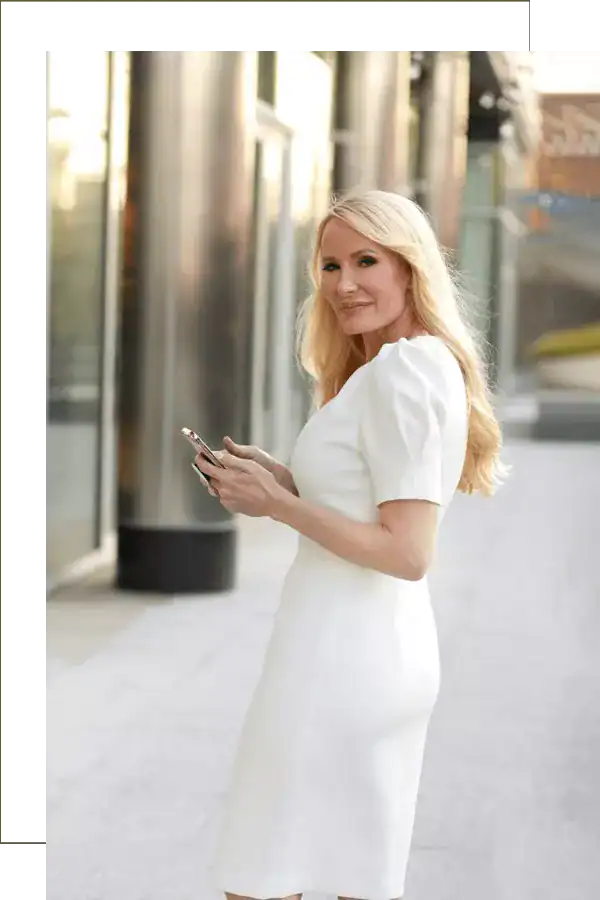 Modern woman in stylish white dress using smartphone outdoors, urban background, professional fashion photography, lifestyle shot, Mia Hewett-inspired image.