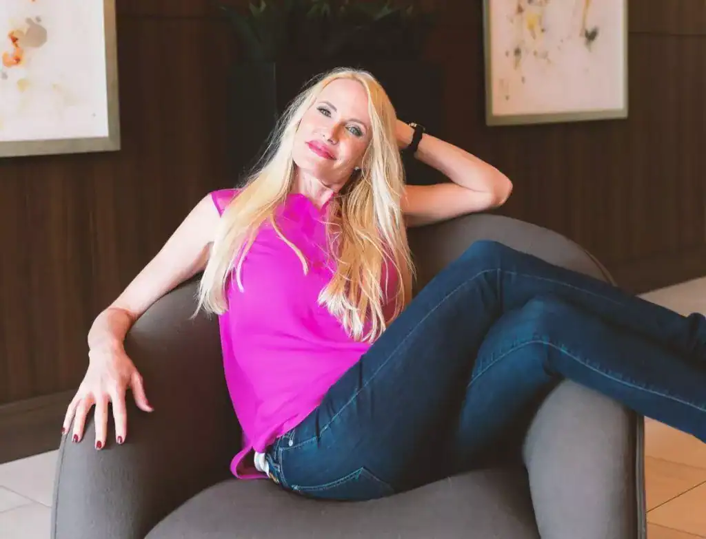 Relaxed woman in pink sleeveless top and dark jeans sitting on a modern couch in stylish interior.