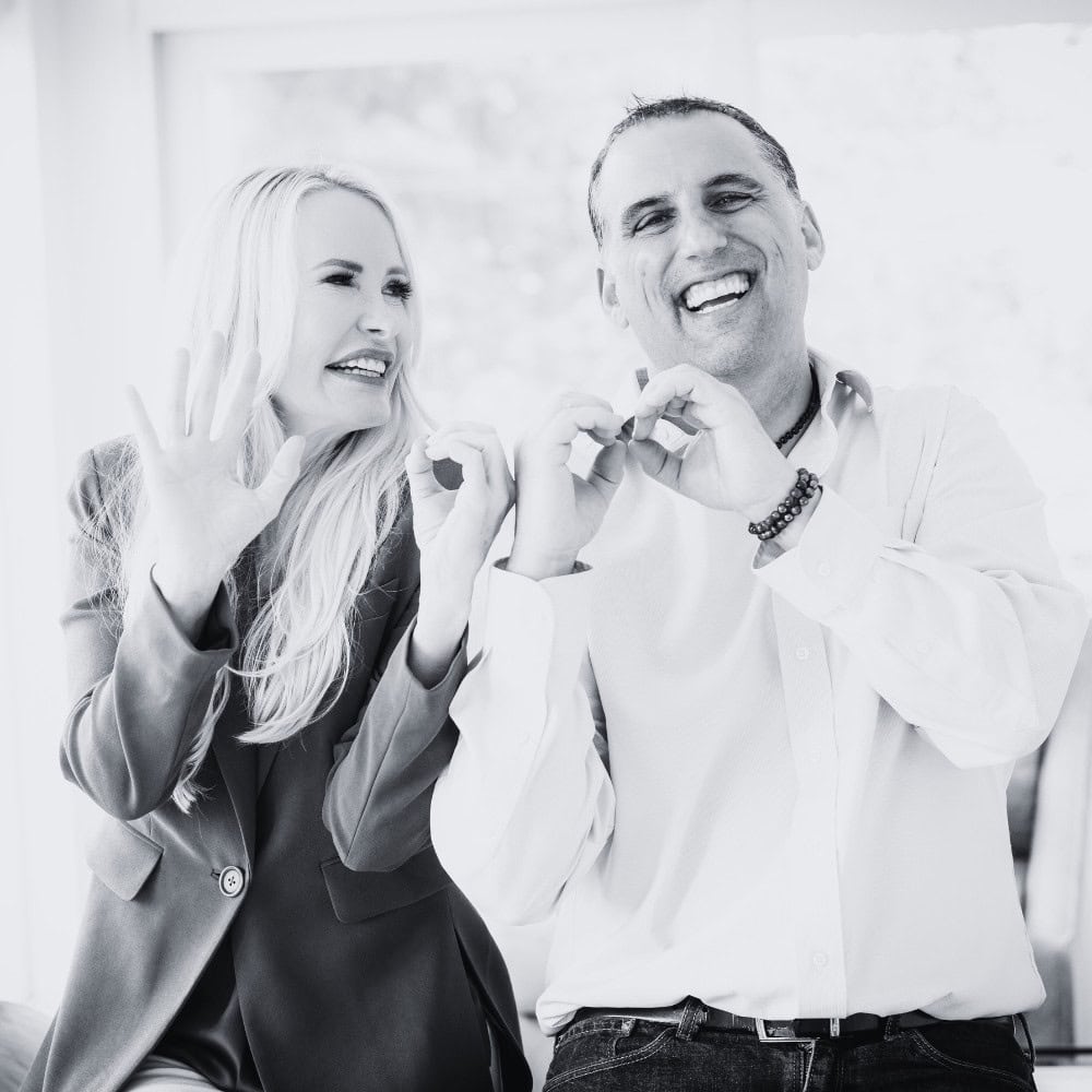 Smiling professional woman and man making heart shape with hands, Black and white photo, celebrating success, friendship, positive energy, modern business environment, Mia Hewett style.