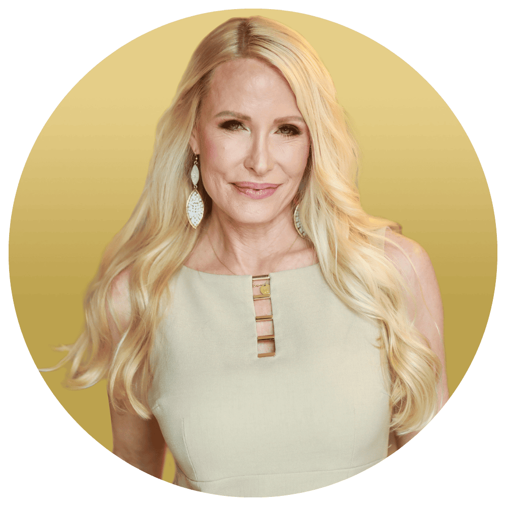 Bright blonde woman smiling in professional headshot, wearing elegant beige dress and statement earrings, representing motivational speaker Mia Hewett and leadership coaching specialist.