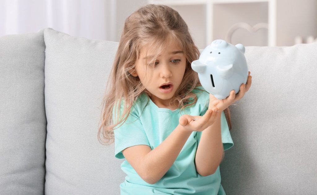 Piggy bank, girl surprised, saving money, financial literacy for kids, child holding piggy bank, learning about money savings, young girl with piggy bank, financial education, kid saving money at home, personal finance for children.