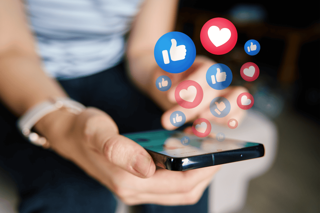 Thumbs up and heart icons floating above a smartphone, symbolizing social media engagement and digital communication. Focus on social media interaction, likes, and online connectivity in a modern digital context.