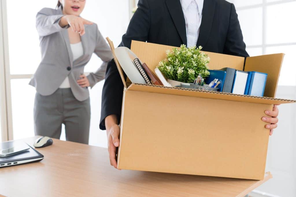 Moving boxes filled with office supplies and a plant, symbolizing work transition or office relocation, in a bright modern workspace.
